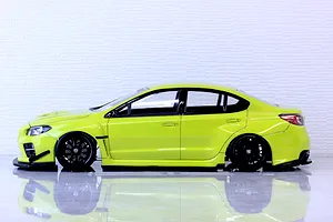 Side profile of a bright yellow RC drift car body shell mounted on a chassis with black multi-spoke wheels against a light background.