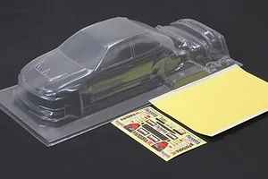 Unpainted clear polycarbonate RC car body shell with a decal sheet and mask sheet on a dark background.
