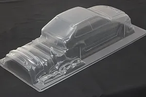 Unpainted clear polycarbonate RC car body shell on a dark background showing molded hatch and front bumper parts.