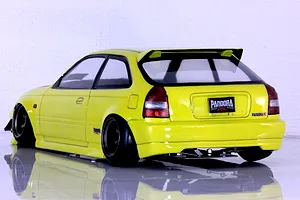 Rear three-quarter studio view of a yellow RC drift car body shell modelled after a Honda Civic EK9 Type-R on a reflective white surface.