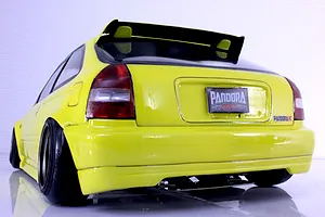 Rear three-quarter view of a yellow Pandora RC Honda Civic EK9 body shell with cambered wheels on a white studio background.