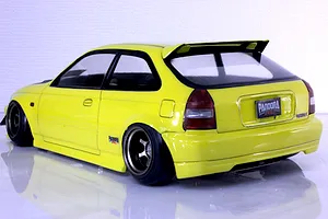 Rear three-quarter view of a bright yellow Honda Civic EK9 Type-R RC drift car body shell with aftermarket wheels and a roof spoiler.