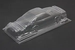 Unpainted clear polycarbonate RC car body shell on a dark grey surface, viewed from a high angle.