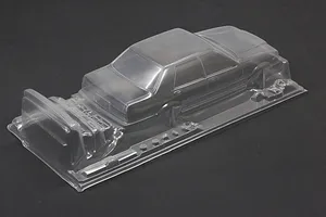 Unpainted clear polycarbonate RC sedan body shell on a dark surface, showing front and side profile details.