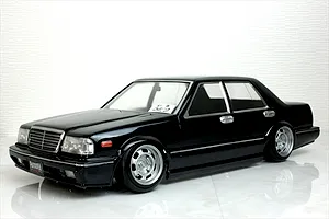 A black RC drift car body shell styled as a classic sedan on a white reflective surface.