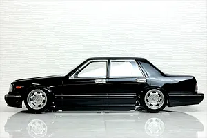 Side profile view of a black RC drift car body shell mounted on a chassis with custom silver wheels, set against a white textured background.