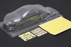 Unpainted clear polycarbonate RC car body shell with window masks and decal sheets on a dark surface.