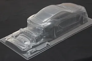 Unpainted clear polycarbonate RC car body shell with additional molded parts on a dark background.