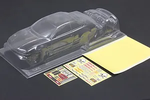 Unpainted clear polycarbonate RC car body shell with separate parts, decal sheets, and mask sheet on a dark surface.
