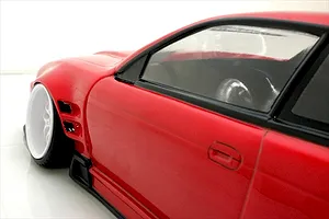 Close-up side profile of a red RC car body showing the front fender, white wheel, side skirts, and window trim.