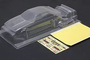 Unpainted clear polycarbonate RC car body shell with a separate spoiler and decal sheet on a dark surface.