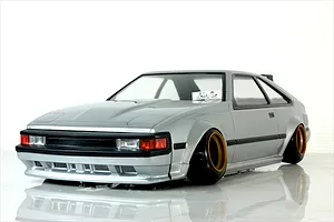 Silver Toyota Celica XX A60 RC drift car body mounted on a chassis with wide gold and black wheels, shown against a plain white background.