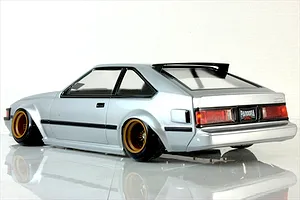 Rear three-quarter view of a silver RC drift car body styled like a classic Toyota Celica on a reflective white studio surface.