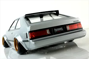 Rear three-quarter studio view of a silver Toyota Celica XX RC drift car body shell with gold-rimmed wheels and a black rear spoiler.