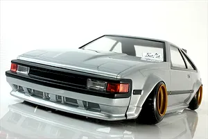 Front three-quarter view of a silver RC drift car body shell resembling a classic Toyota Celica parked on a reflective white studio surface.