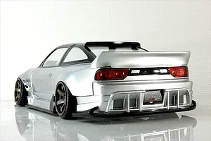Rear quarter view of a silver RC drift car body shell, featuring a large rear wing, detailed taillights, and wide wheels against a white background.