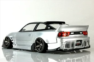Rear-three-quarter view of a painted silver RC drift car body shell mounted on a chassis with bronze wheels.
