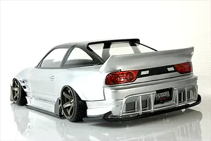 Rear-three-quarter view of a silver RC drift car body shell mounted on a chassis with bronze wheels against a white background.