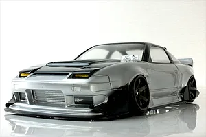 Low angle front three-quarter view of a silver and black Pandora RC RPS13 180SX drift car body shell with custom aero kit and wheels on a reflective white surface.