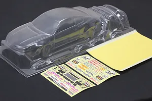 Clear unpainted RC car body shell with separate parts, decal sheet, and window mask sheet on a dark background.