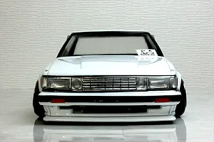 Front view of a white RC drift car body shell, showing detailed grille, headlights, and a sticker on the windshield against a neutral background.