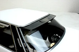 Close-up of a dark rear window visor spoiler fitted to a white RC model car body shell against a light background.