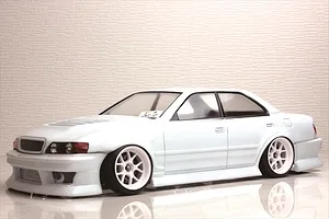 White Toyota Chaser RC drift car body shell with deep dish wheels on a reflective surface against a textured background.