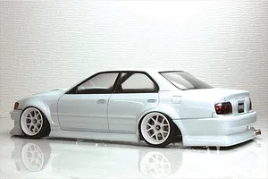 Side view of a painted white Toyota Chaser JZX100 RC drift car body shell with white multi-spoke wheels on a reflective surface.