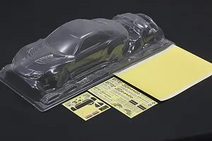 Unpainted clear polycarbonate RC car body shell with separate decal sheets and window masks on a dark surface.