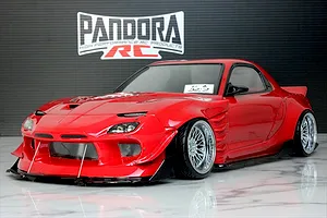 Red RC drift car body shell of a Mazda RX-7 FD3S with wide body kit and chrome mesh wheels displayed indoors.