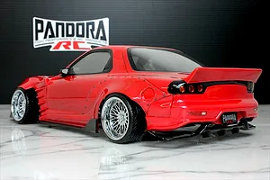 Rear-three-quarter view of a painted red Mazda RX-7 FD3S RC drift car body with widebody fenders and chrome mesh wheels.