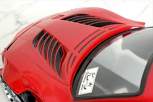 Close-up of the red RC car body bonnet featuring black vents and a windshield sticker against a white marble background.