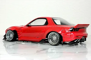 Rear-three-quarter studio shot of a red Mazda RX-7 RC drift car body with wide body kit and chrome mesh wheels.