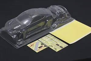 Unpainted clear RC car body shell with accessory parts and sticker sheets on a black surface