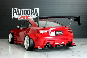 Rear view of a painted red Pandora RC Toyota 86 body shell with a large black wing, wide fenders, and Pandora RC logo in the background.