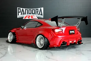 Rear-three-quarter view of a painted red Toyota 86 RC drift car body shell with a large rear wing, widebody fenders, and Pandora RC logo backdrop.