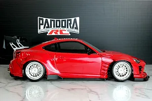 Side profile of a red Toyota 86 RC drift car body with wide fenders, large rear wing, and silver mesh wheels.