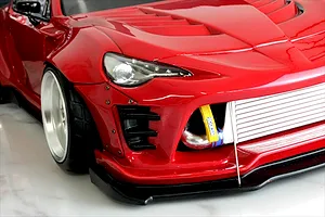 Close-up front quarter view of a red RC drift car body showing the front bumper, intercooler, and wide-body fender.
