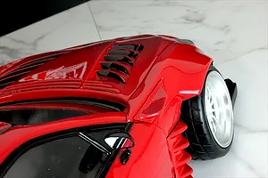 Close-up of a glossy red RC car body showing the front fender, louvered hood vents, side mirror, and front wheel.