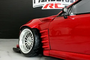Close-up of the front wheel arch and fender of a red radio-controlled drift car body with wide body kit and deep dish wheel.
