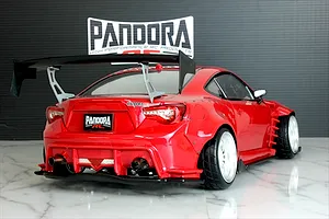 Rear view of a red RC drift car with a large black wing, wide body kit, and Pandora RC logo in the background.