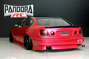 Rear three-quarter view of a painted red RC drift car body featuring black wheels, dual exhaust, and Pandora RC branding on a studio background.