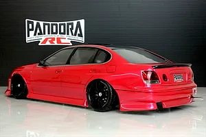 Rear three-quarter view of a painted red RC drift car body shell mounted on a chassis with black wheels against a black branded backdrop.