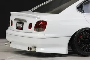 Close-up of the rear section of a white RC drift car body shell, showing tail lights, twin exhaust tips, rear spoiler, and black wheel.