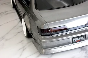 Rear corner view of a silver RC drift car body shell featuring tinted tail lights and a Pandora RC license plate on a marble surface.