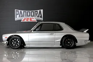 Side profile view of a silver Pandora RC KPGC10 Skyline GT-R body shell mounted on an RC chassis with black wheels, set against a dark background.