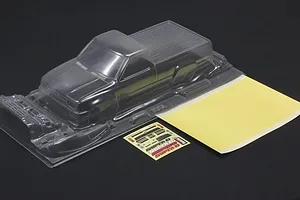 Unpainted clear polycarbonate RC truck body shell with a mask sheet and decal sheet on a dark background.