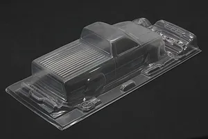 Unpainted clear polycarbonate RC truck body shell for Toyota Hilux with separate accessories on a dark background.