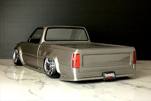 Rear-three-quarter view of a customized silver RC pickup truck body shell with lowered stance, custom wheels, and Pandora RC license plate.