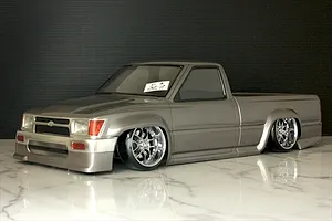 Silver painted Toyota Hilux RC drift truck body shell on a reflective marble surface against a dark background.
